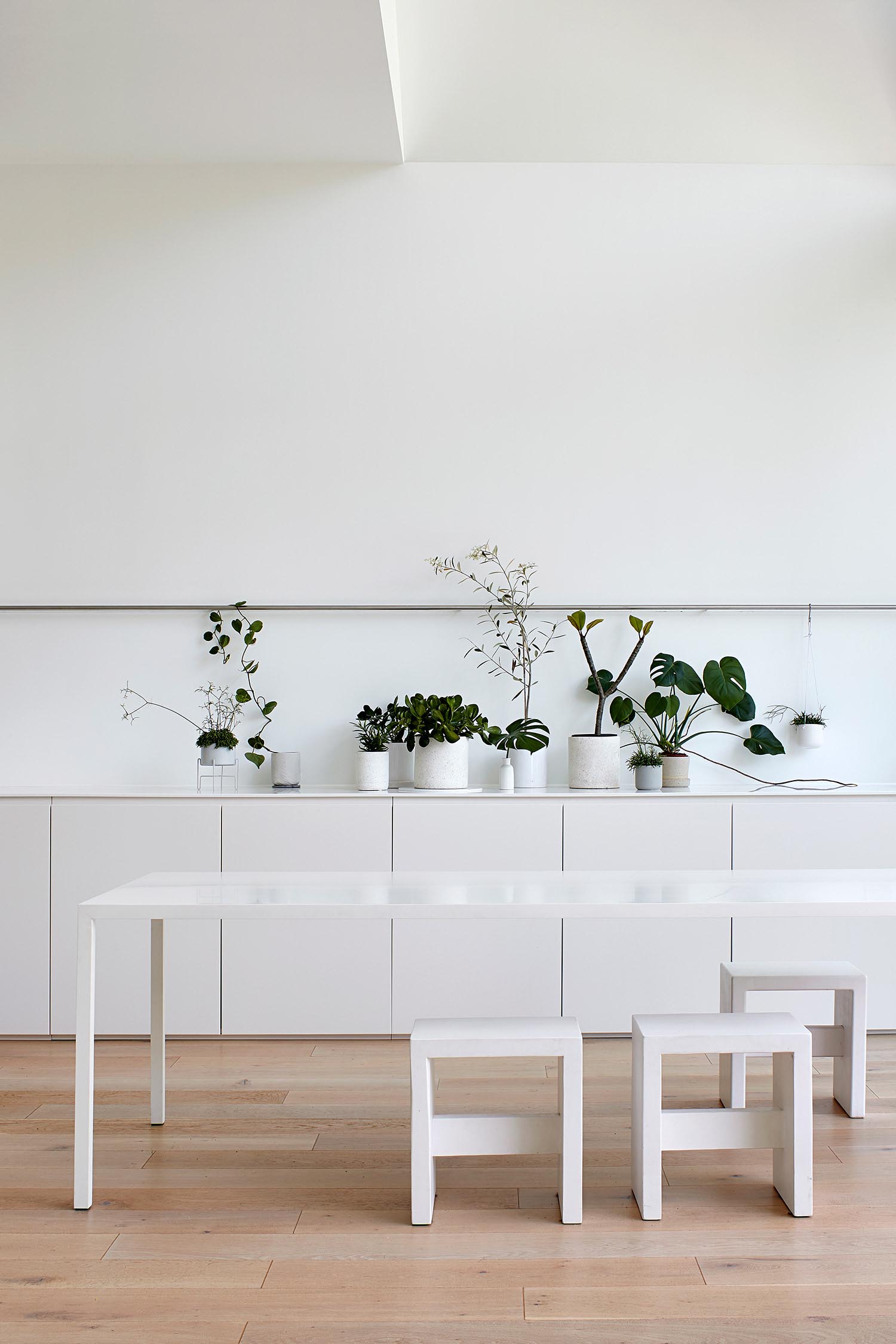 Современная столовая с минималистичной белой мебелью и горшками для украшения.