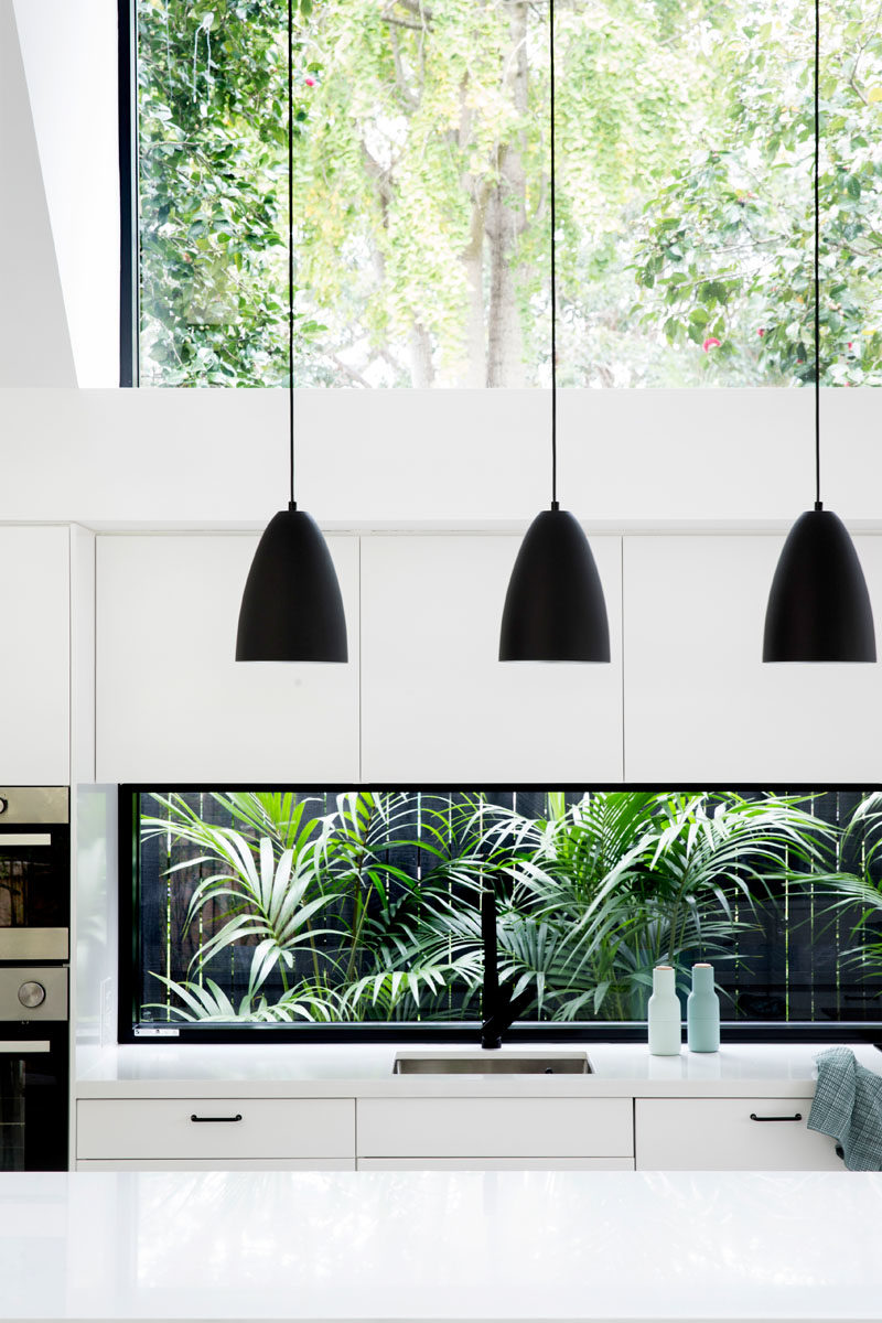 Идеи для кухни - в этой современной кухне три черных подвесных светильника над островом привлекают взгляд вверх, чтобы выделить потолок двойной высоты, а белые шкафы помогают кухне сливаться с белыми стенами. #KitchenDesign #KitchenIdeas #WhiteKitchen