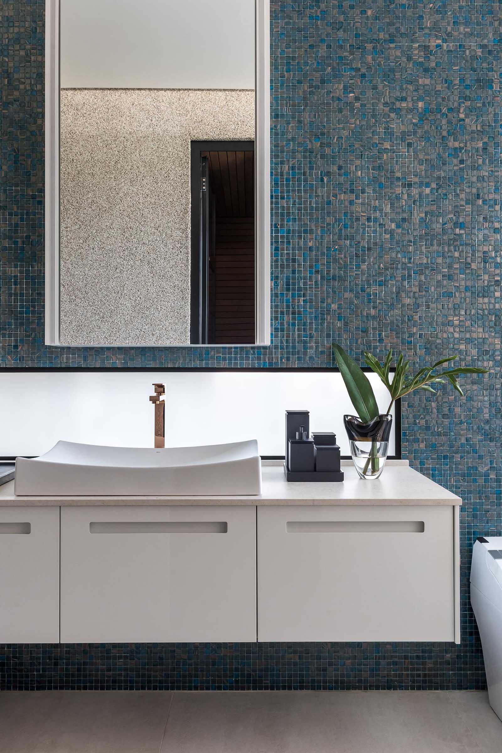Акцентная стена, выложенная синей плиткой, служит фоном для белого туалетного столика и зеркала в этой современной ванной комнате.