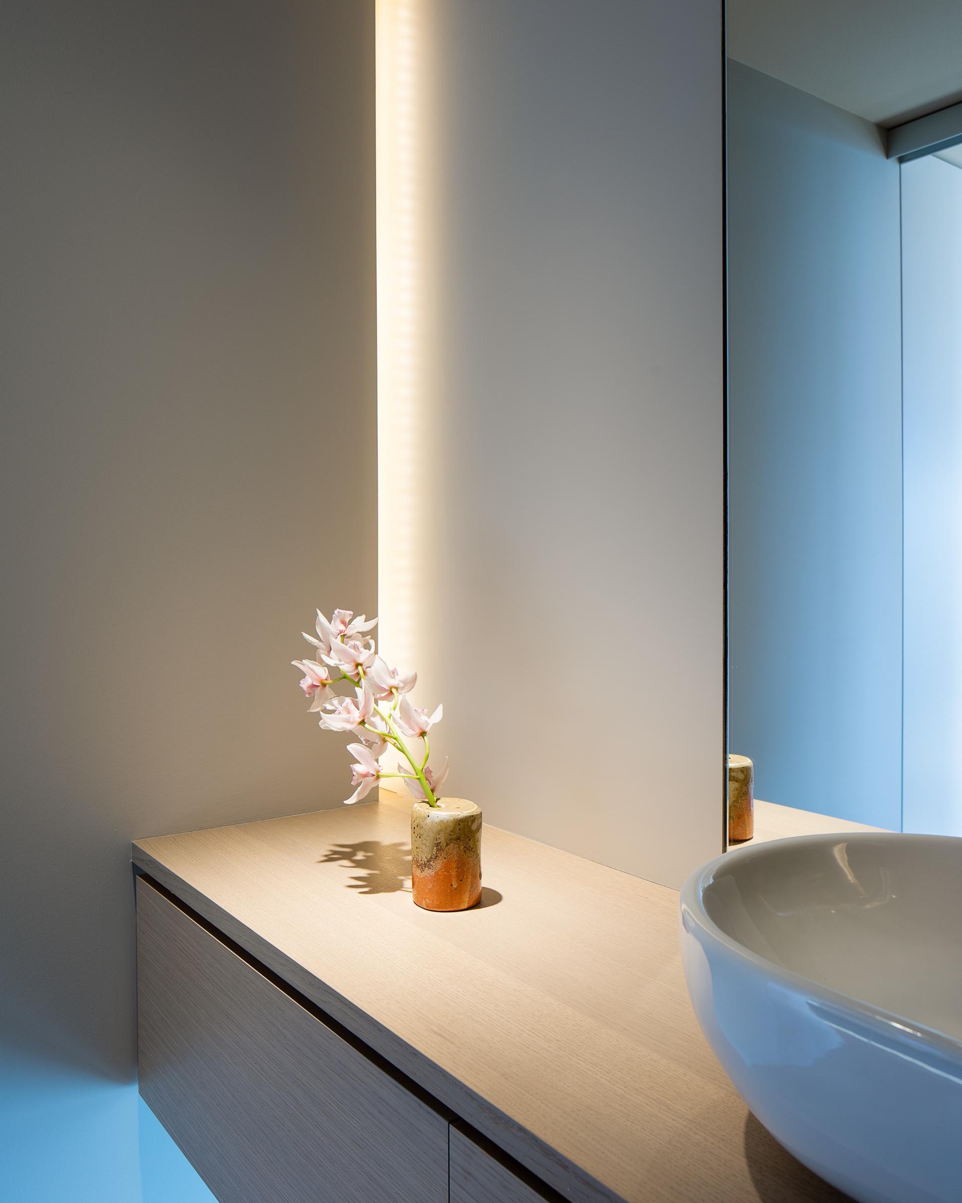 В этой современной ванной комнате есть парящий деревянный туалетный столик со скрытым освещением, спрятанным в углу.