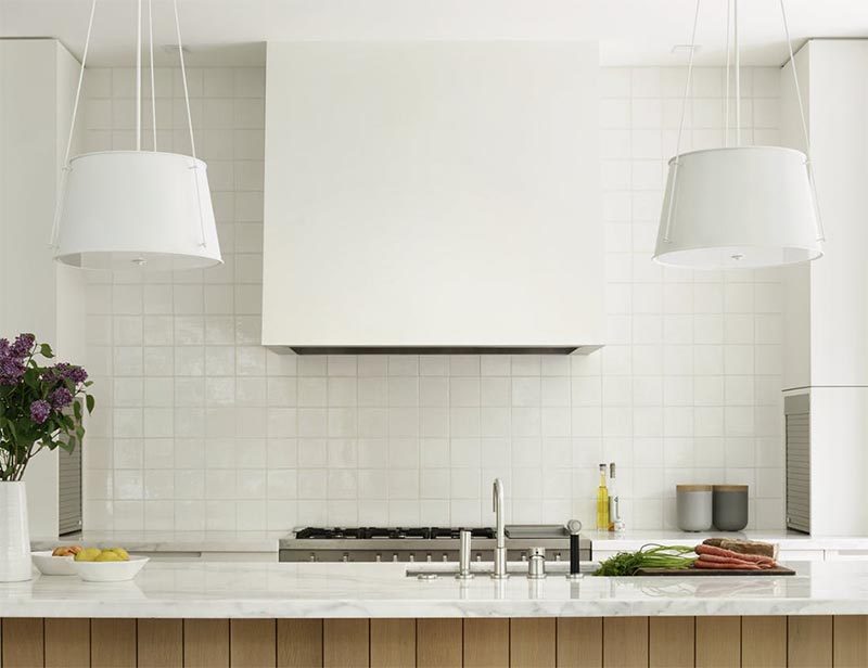 Эта современная кухня оснащена двумя подвесными светильниками, раковиной под столешницей, фартуком из белой плитки, приборами из нержавеющей стали и вытяжкой, подходящей к шкафам. # СовременнаяКухня #KitchenDesign # БелаяКухня