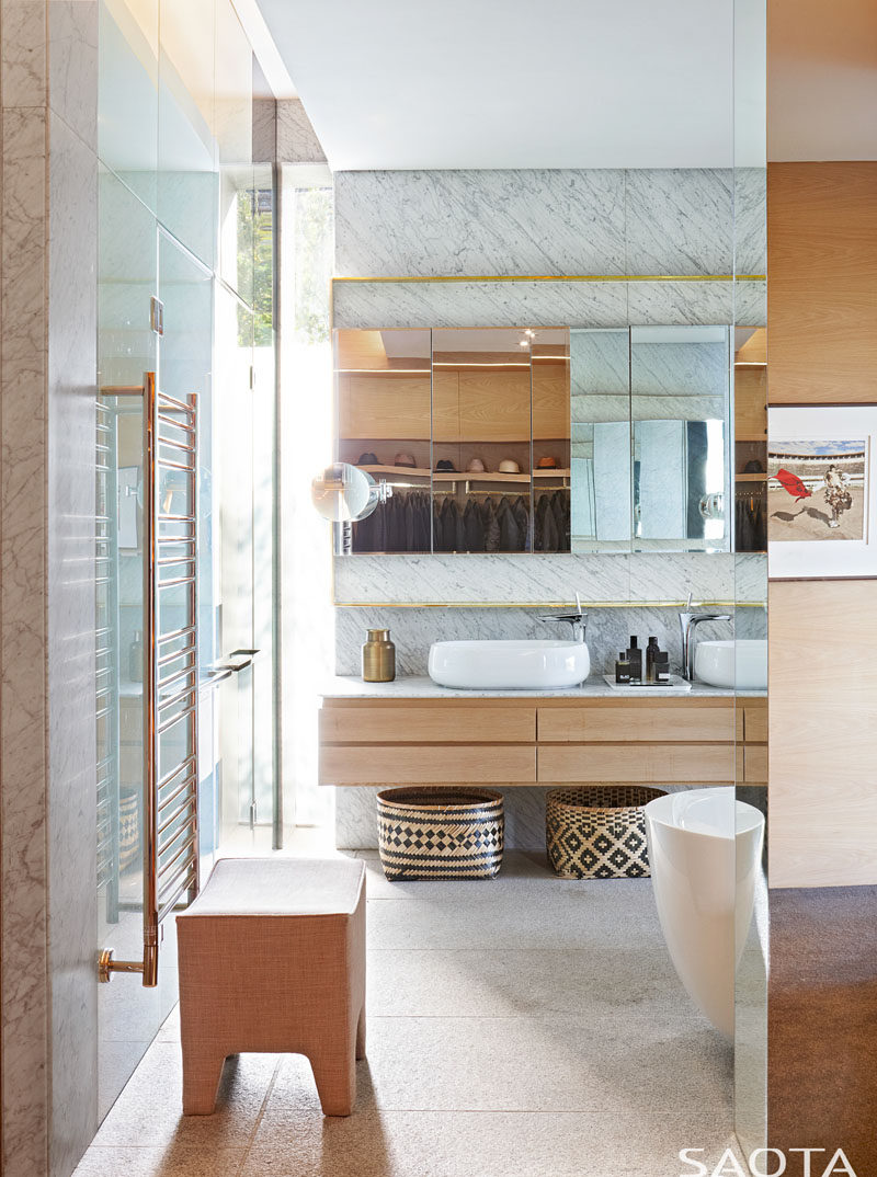 Эта современная ванная комната украшена золотыми вставками, камнем, стеклом, деревом и белыми раковинами, которые дополняют белую отдельно стоящую ванну. # Современная ванная # Дизайн ванной
