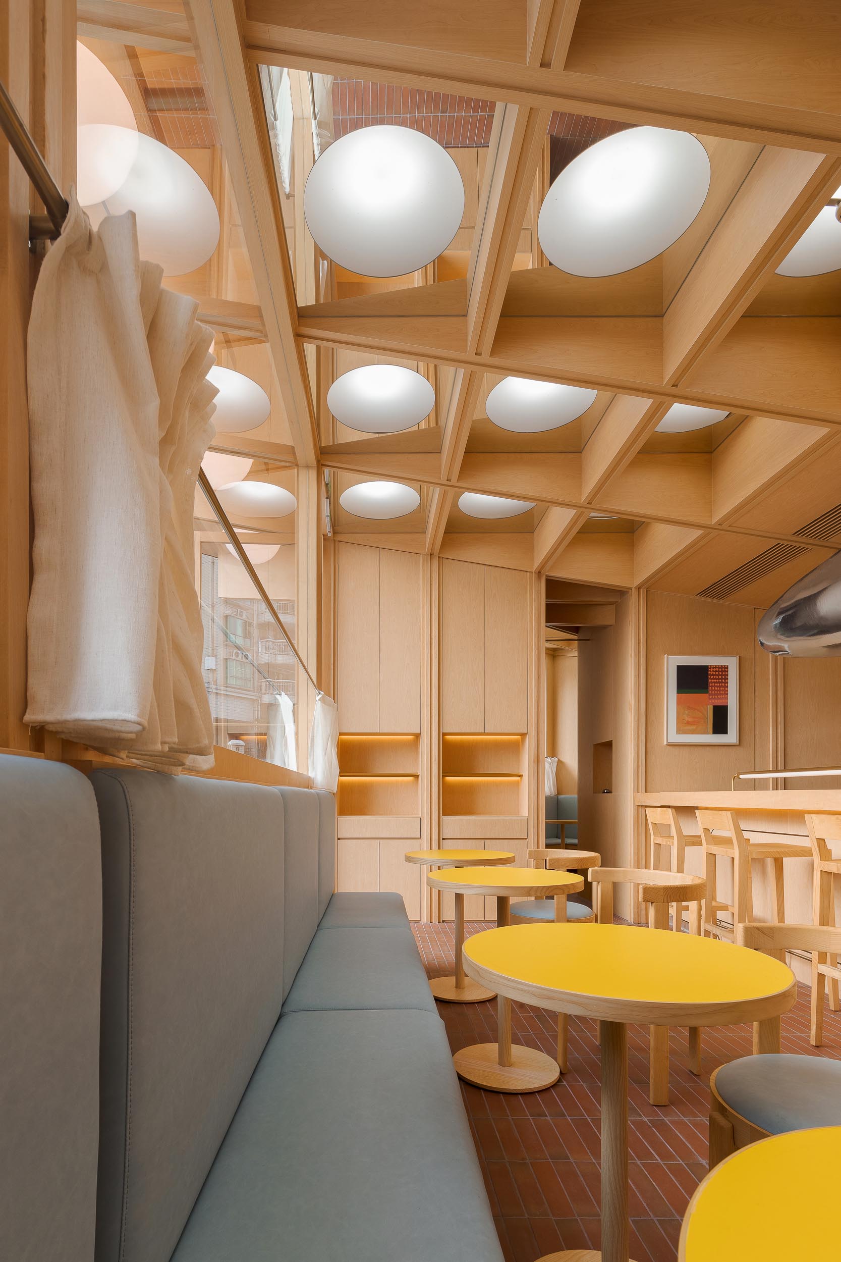 Современное кафе и бар с деревянным интерьером, банкетными креслами и ярко-желтыми столиками.