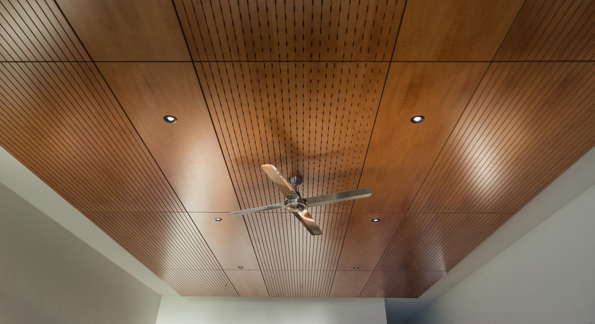 Интерьер открытой планировки с деревянным акцентом на потолке и скрытой подсветкой.