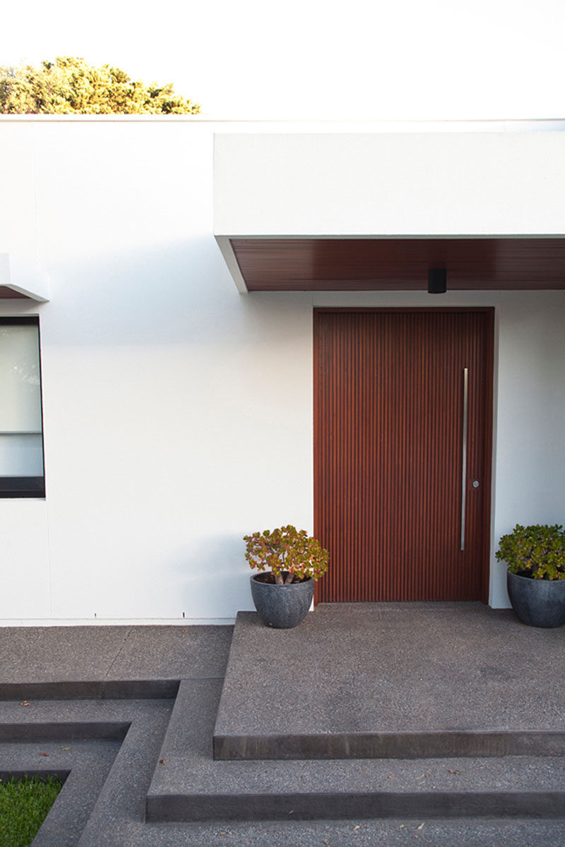 Дверь из темного дерева, ведущая в этот австралийский дом, имеет вертикальные линии, а высокая, тонкая, вертикально расположенная металлическая дверная ручка в минималистском стиле повторяет линии в дереве.