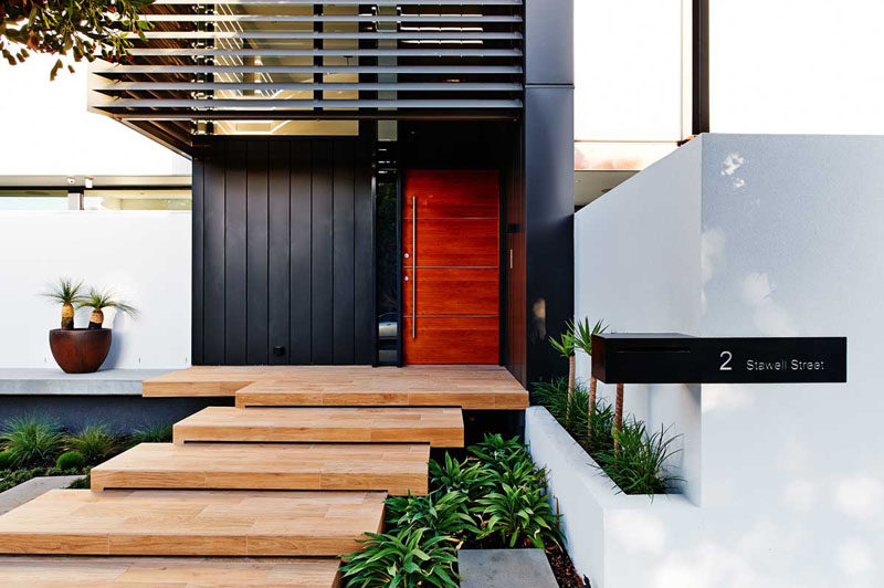 Эта большая деревянная дверь, состоящая из четырех деревянных панелей и серебряной металлической дверной ручки, согревает черные металлические панели и придает современный вид экстерьеру этого австралийского дома.