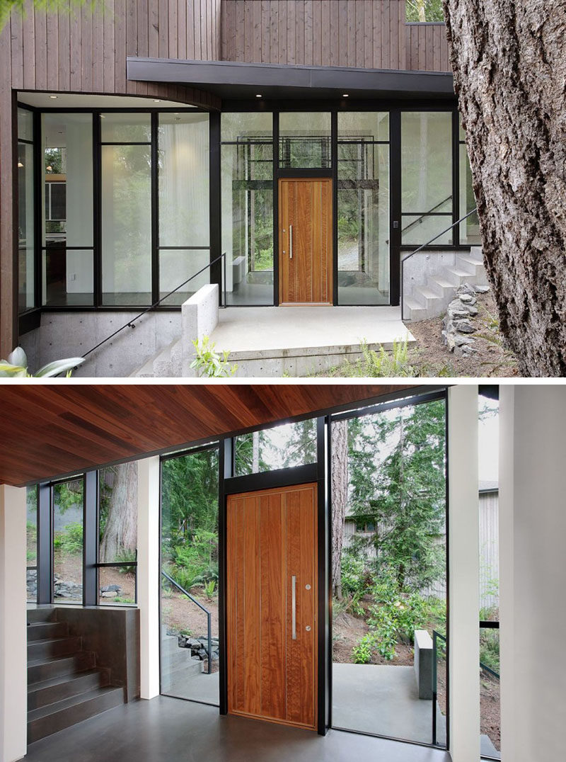 Эта дверь, обшитая панелями из светлого дерева, с серебряной дверной ручкой, окружена стеной с окнами и черными стальными рамами, которые создают современный вход, наполненный естественным светом.