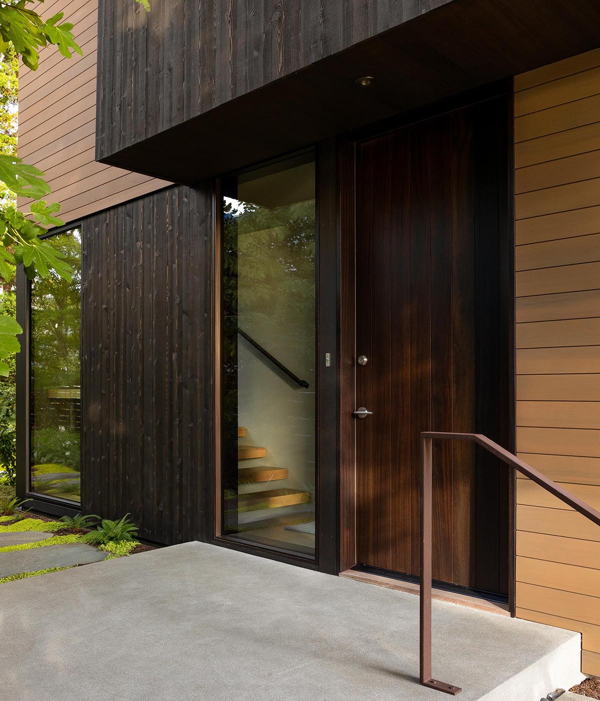 Черный деревянный сайдинг и темная входная дверь приветствуют посетителей этого современного дома.