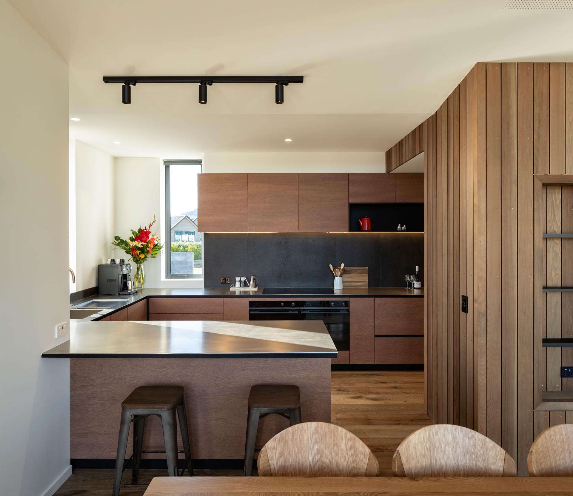 Современная кухня с минималистскими шкафами из теплого дерева в сочетании с серым фартуком и темными столешницами создает современный вид.