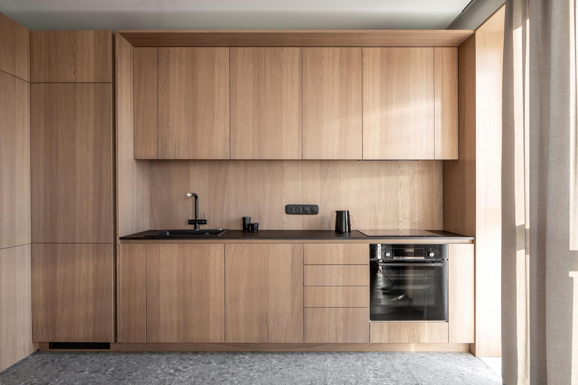 Современная деревянная кухня со шкафами без оборудования, а также встроенным холодильником и посудомоечной машиной.
