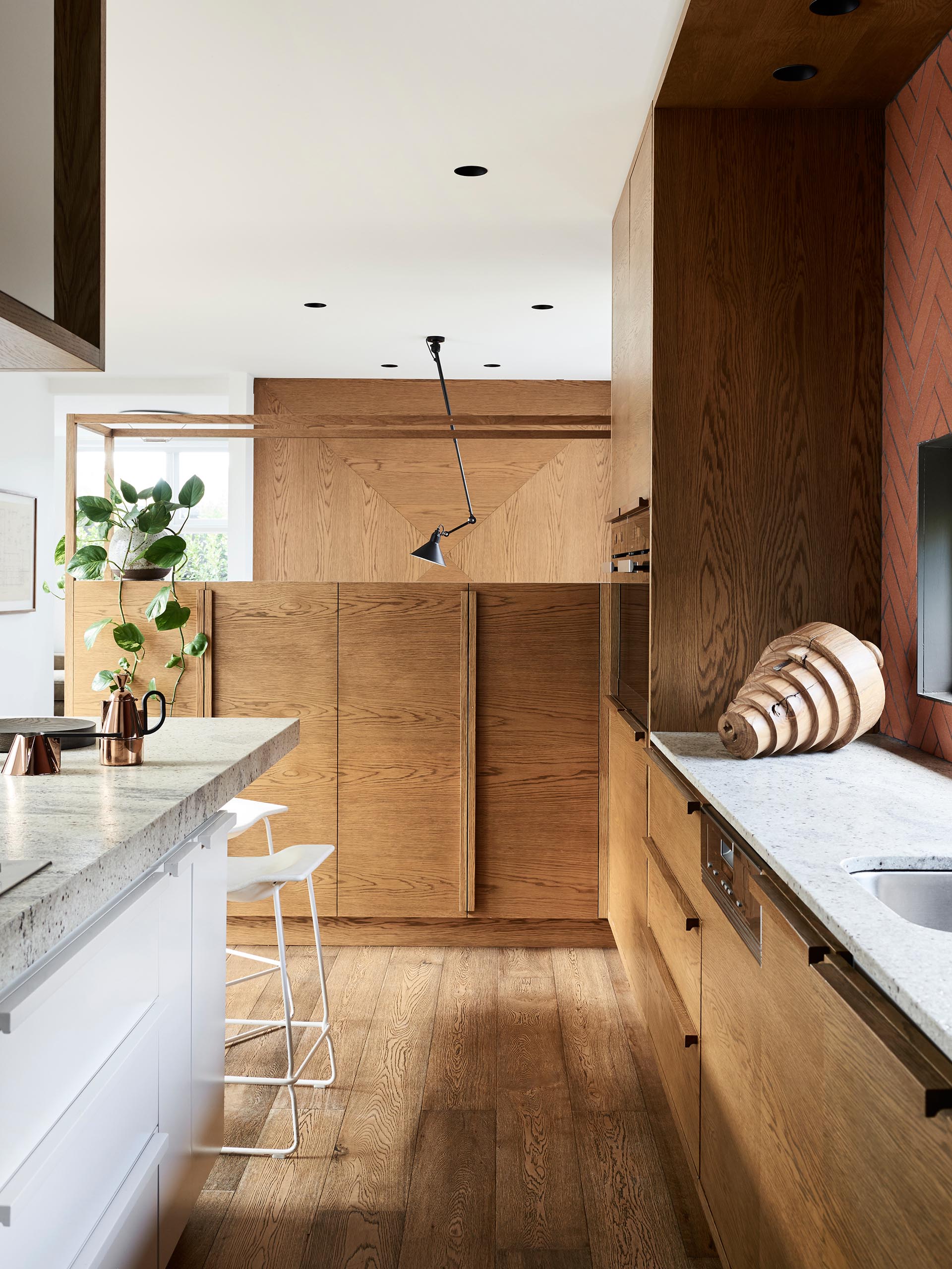 Эта кухня отделана деревом в минималистском стиле, а белые шкафы сочетаются с длинным островом и плиточным фартуком терракотового цвета, окружающим окно.