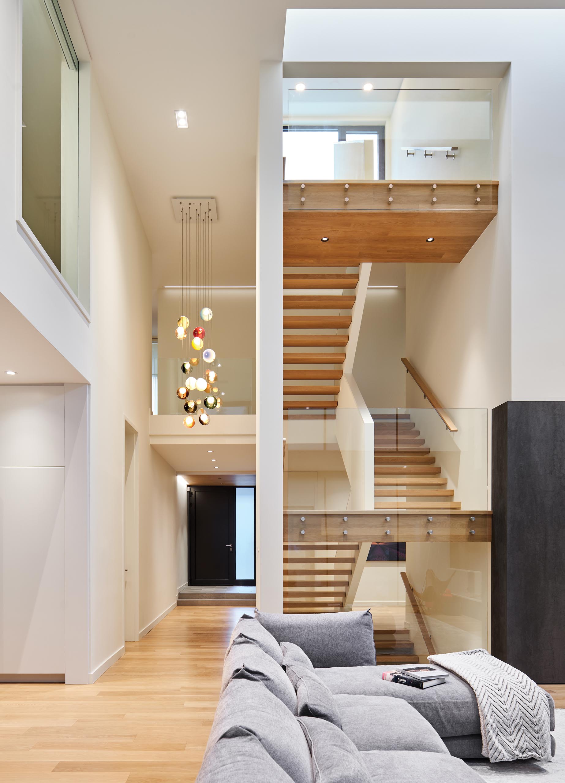 Открытая деревянная лестница со стеклянными перилами, соединяющая несколько уровней дома. Яркий акцент был добавлен подвесными фарами Bocci.