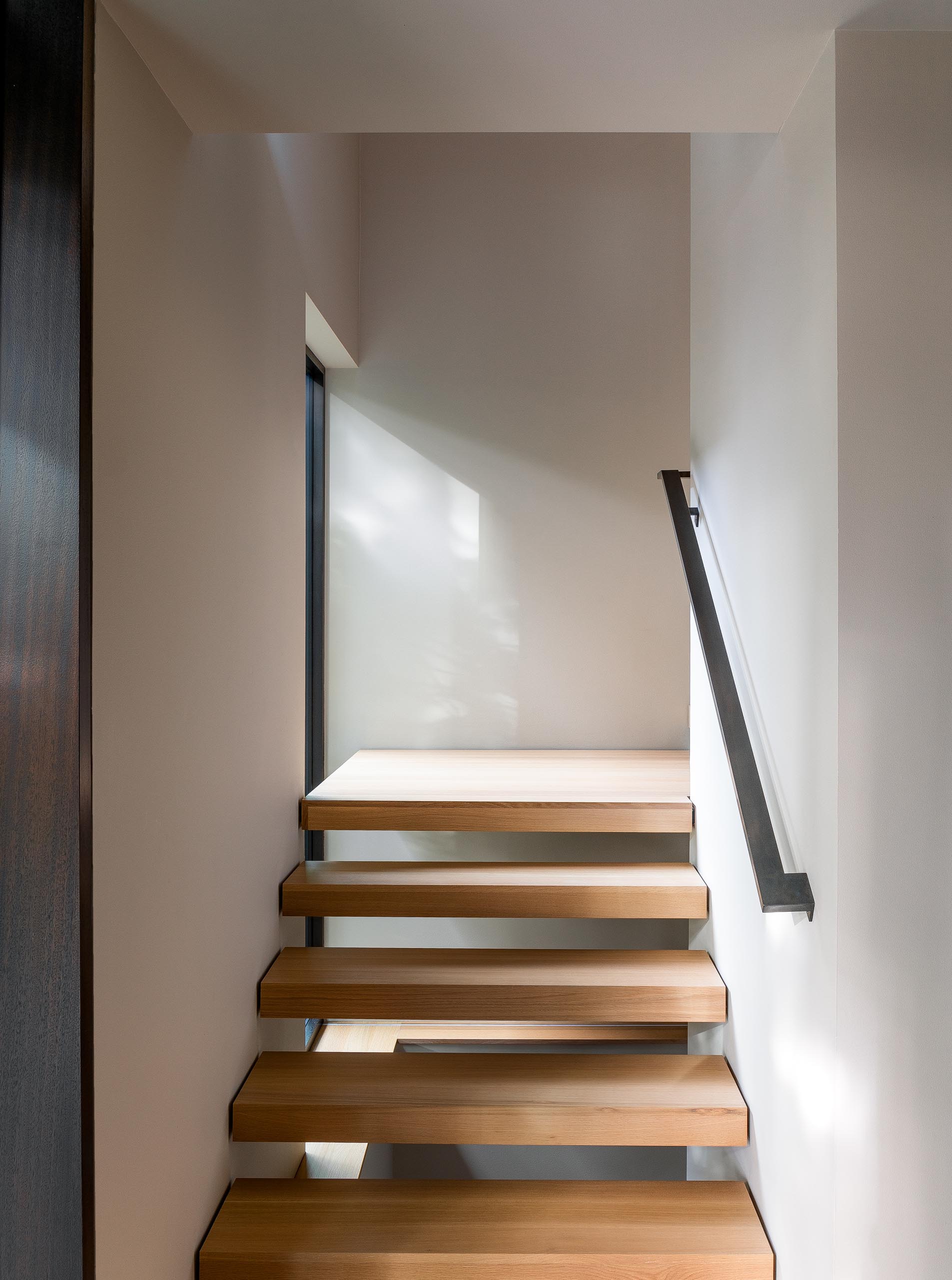 Деревянная лестница соединяет верхние социальные зоны этого современного дома со спальнями и ванными комнатами, расположенными на нижнем уровне.
