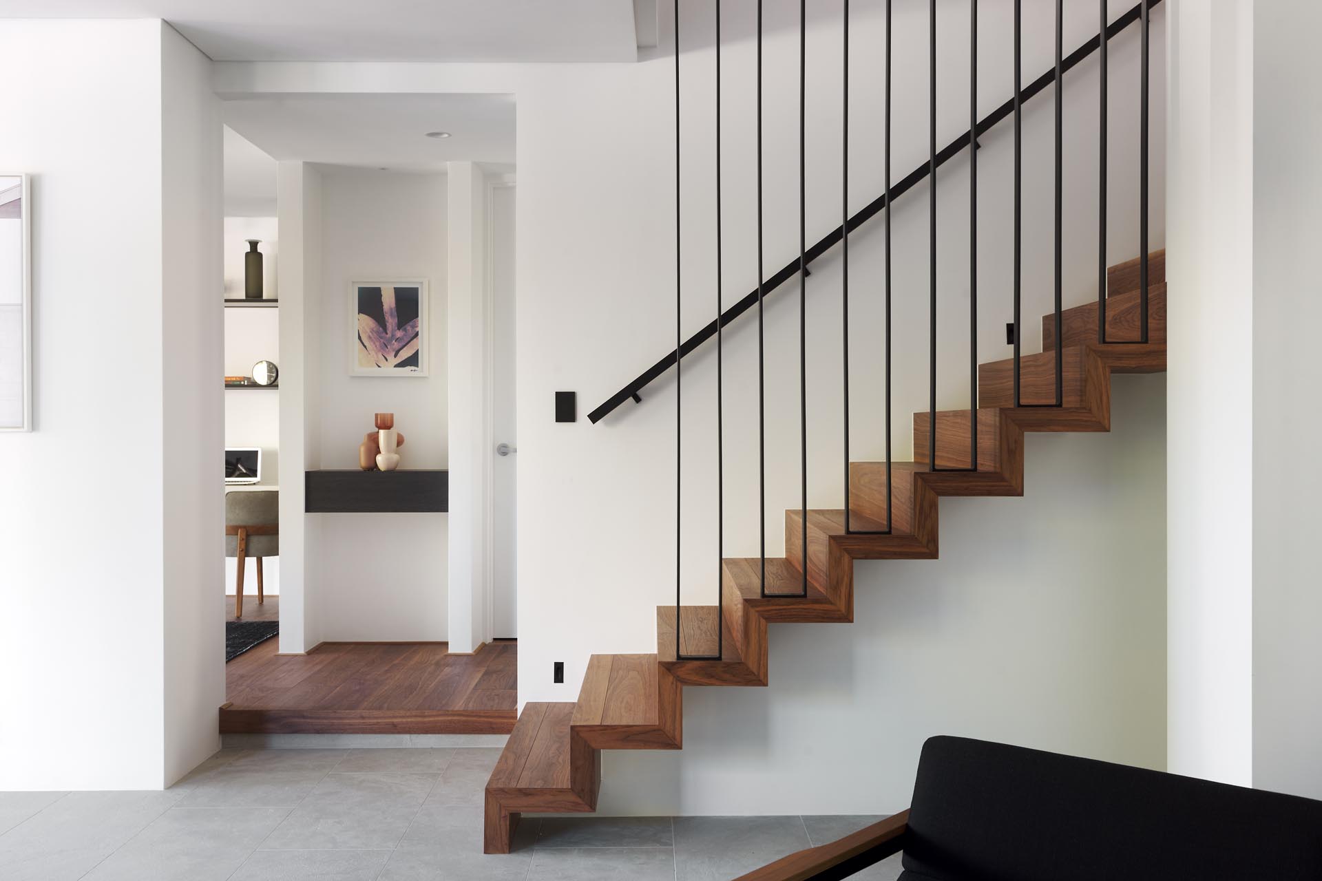 Современный интерьер дома с деревянной лестницей с черными металлическими перилами, ведущими на верхний этаж дома.