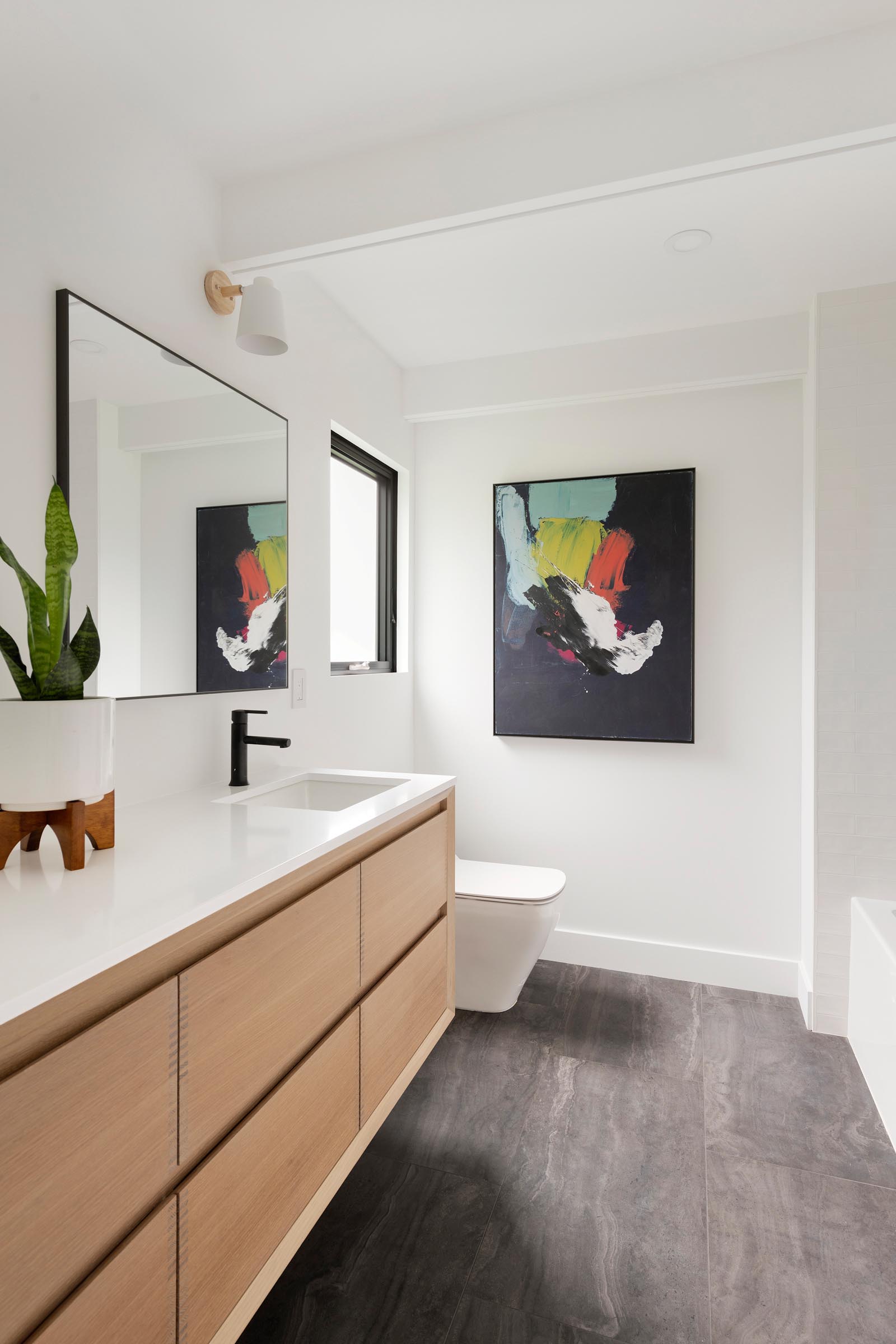 В этой современной ванной комнате белые стены и туалетный столик из светлого дерева делают пространство ярким, а произведения искусства добавляют яркости.