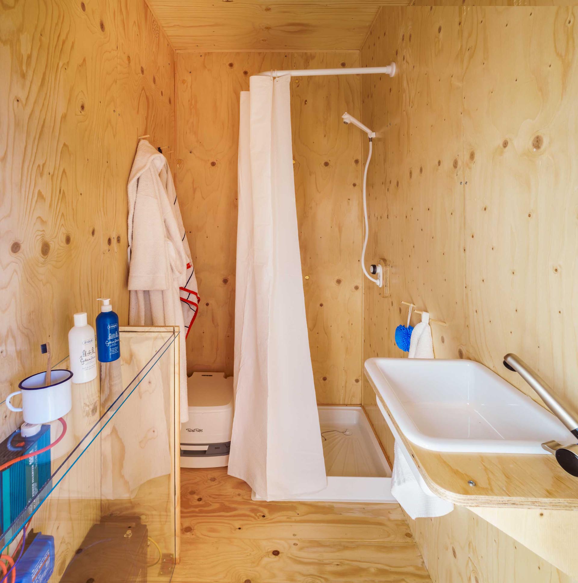 В крохотном доме из транспортного контейнера есть облицованная фанерой ванная комната с душем.