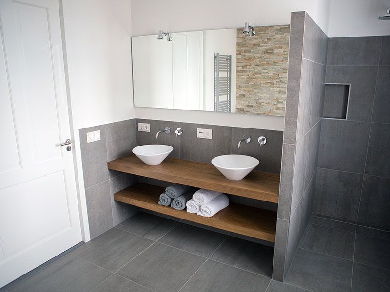 Идеи дизайна ванной комнаты - открытая полка под столешницей // Эта ванная комната преимущественно покрыта каменной плиткой, но утеплена деревянной стойкой и полкой, которые придают ей современный и привлекательный вид.