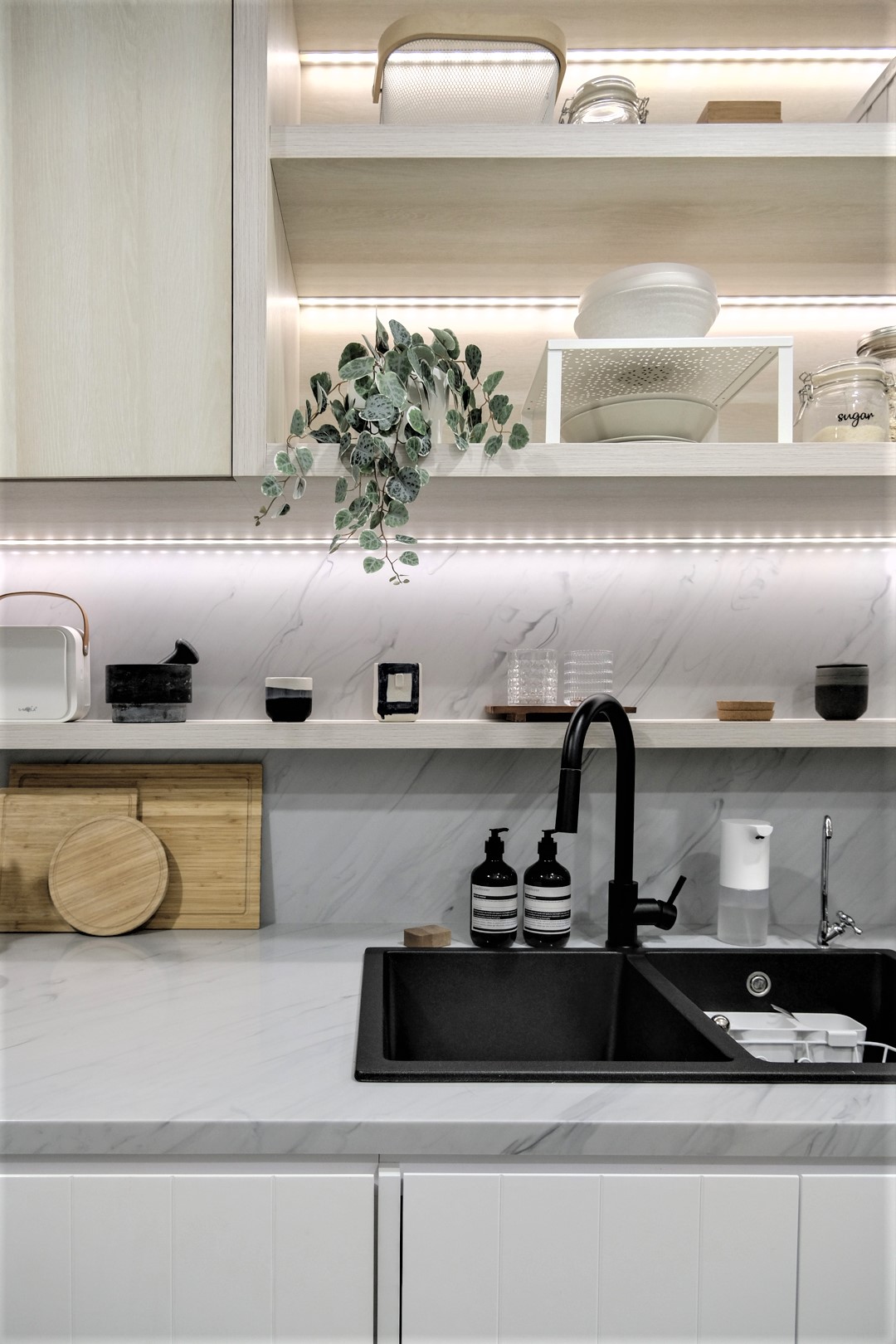 Небольшая кухня квартиры, спроектированная со шкафами из светлого дерева, имеет полосы светодиодного освещения, которые сохраняют пространство ярким.