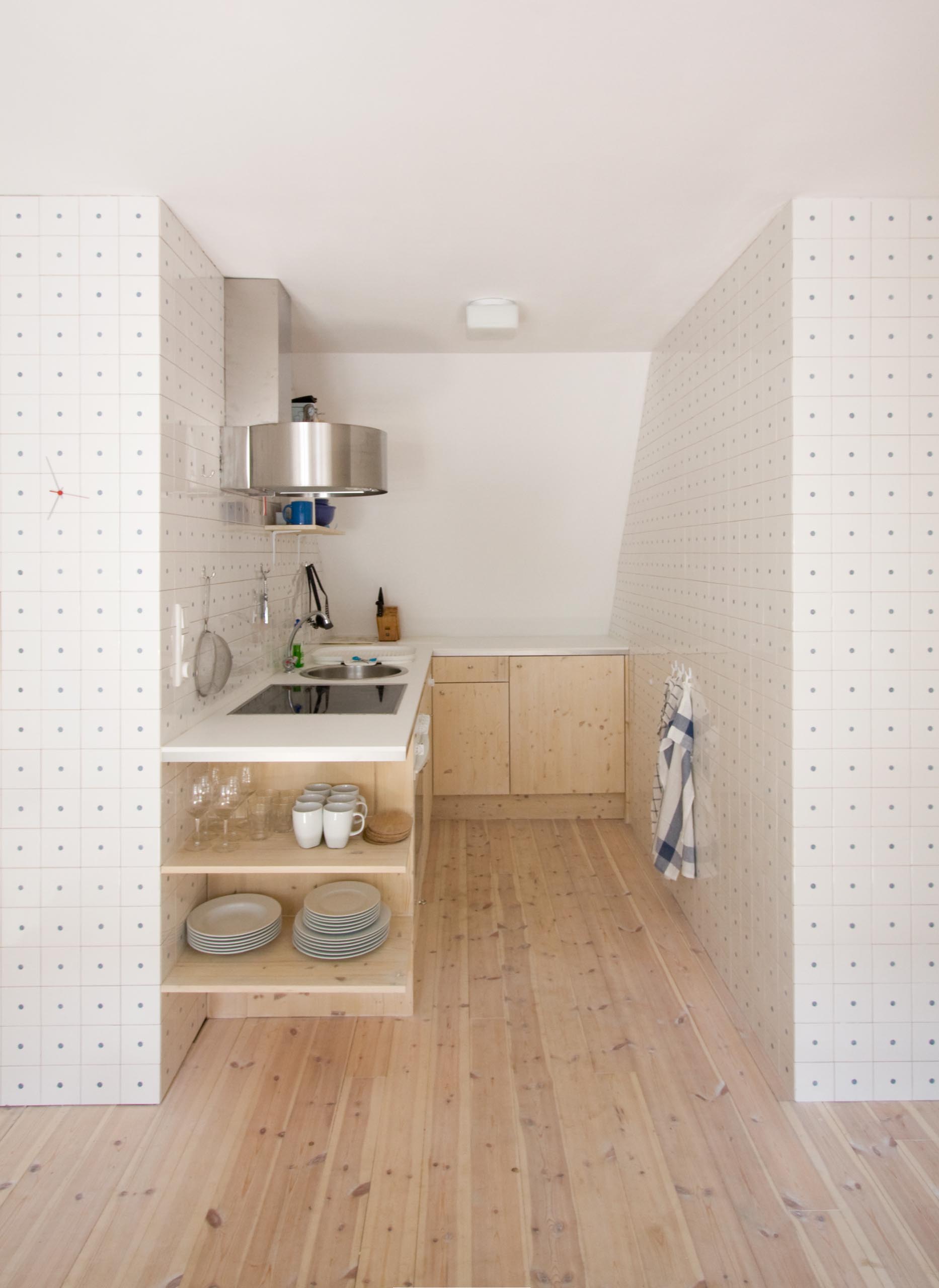 Простая небольшая кухня с сосновыми полами и шкафчиками и белой столешницей.