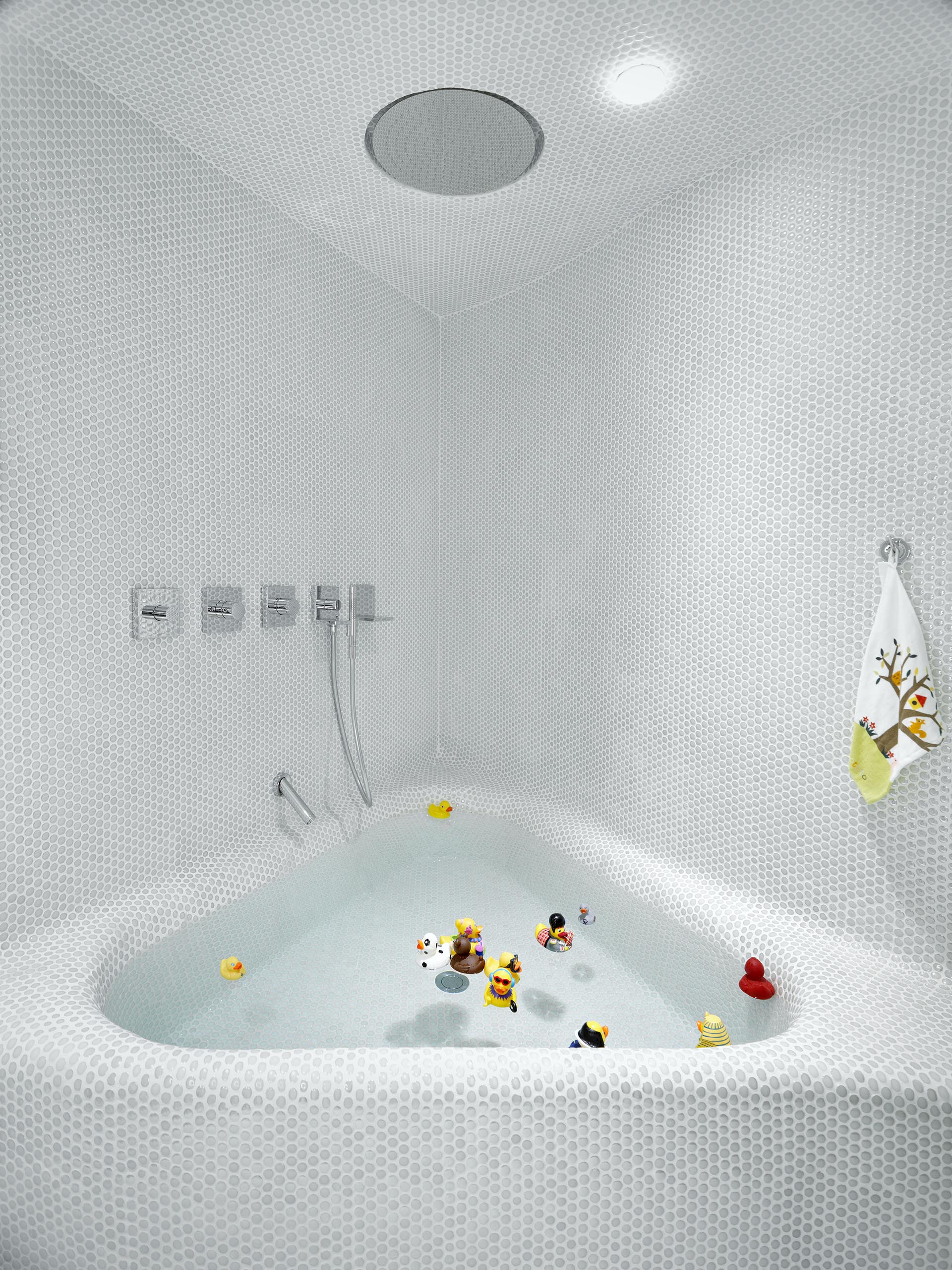 Современная белая ванная комната с мелкой плиткой и встроенной треугольной ванной.