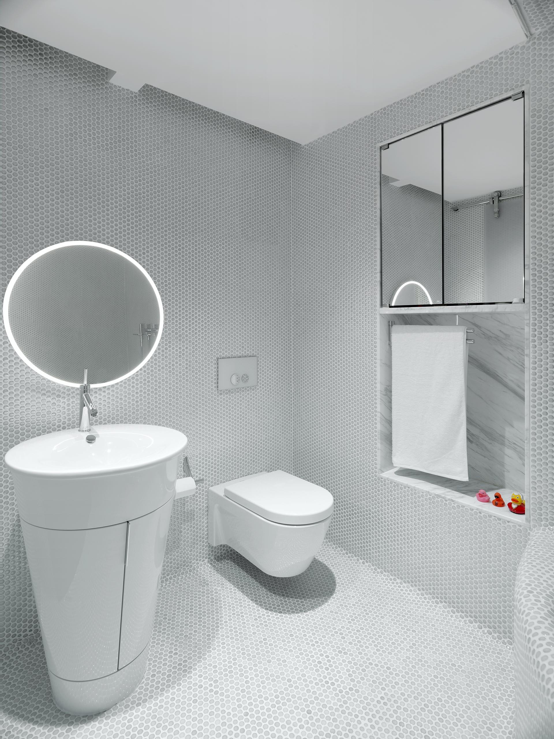 Белая ванная комната, облицованная пенни плиткой, также имеет встроенное зеркало и нишу для стеллажей.